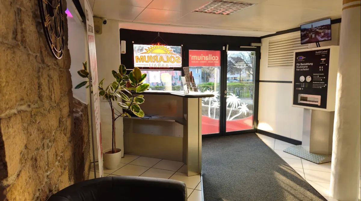 Eingangsbereich mit dem beleuchteten Schriftzug Solarium Aarau, Empfangstresen und dem Studio-Control-Terminal